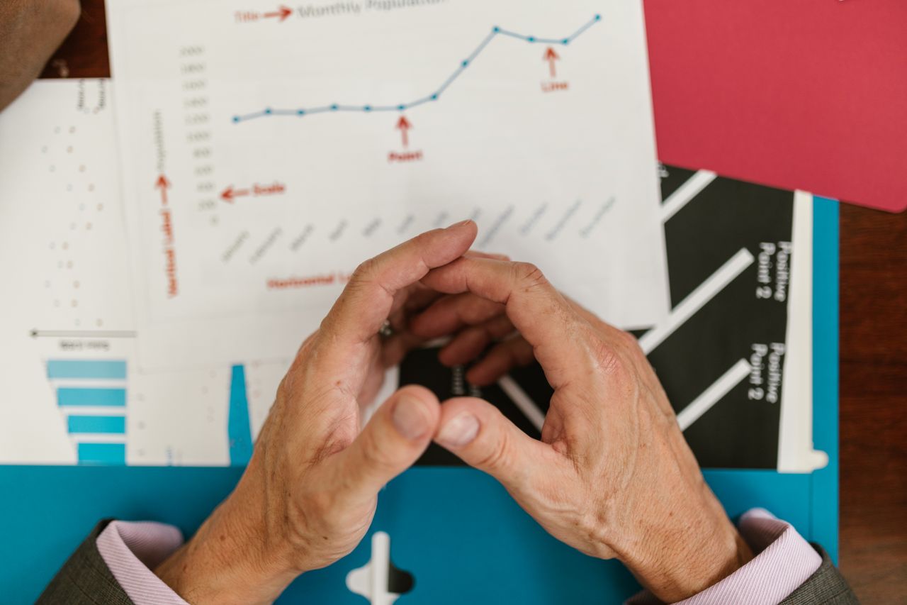 about-us-01 Hands examining financial graphs and charts on a wooden desk, indicative of business planning.